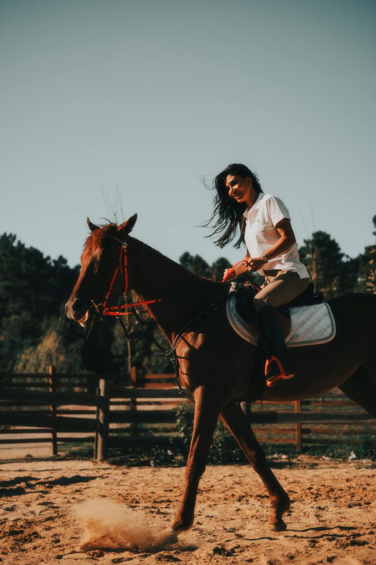 Woman enjoys horseback riding in a sunny outdoor area with natural surroundings.